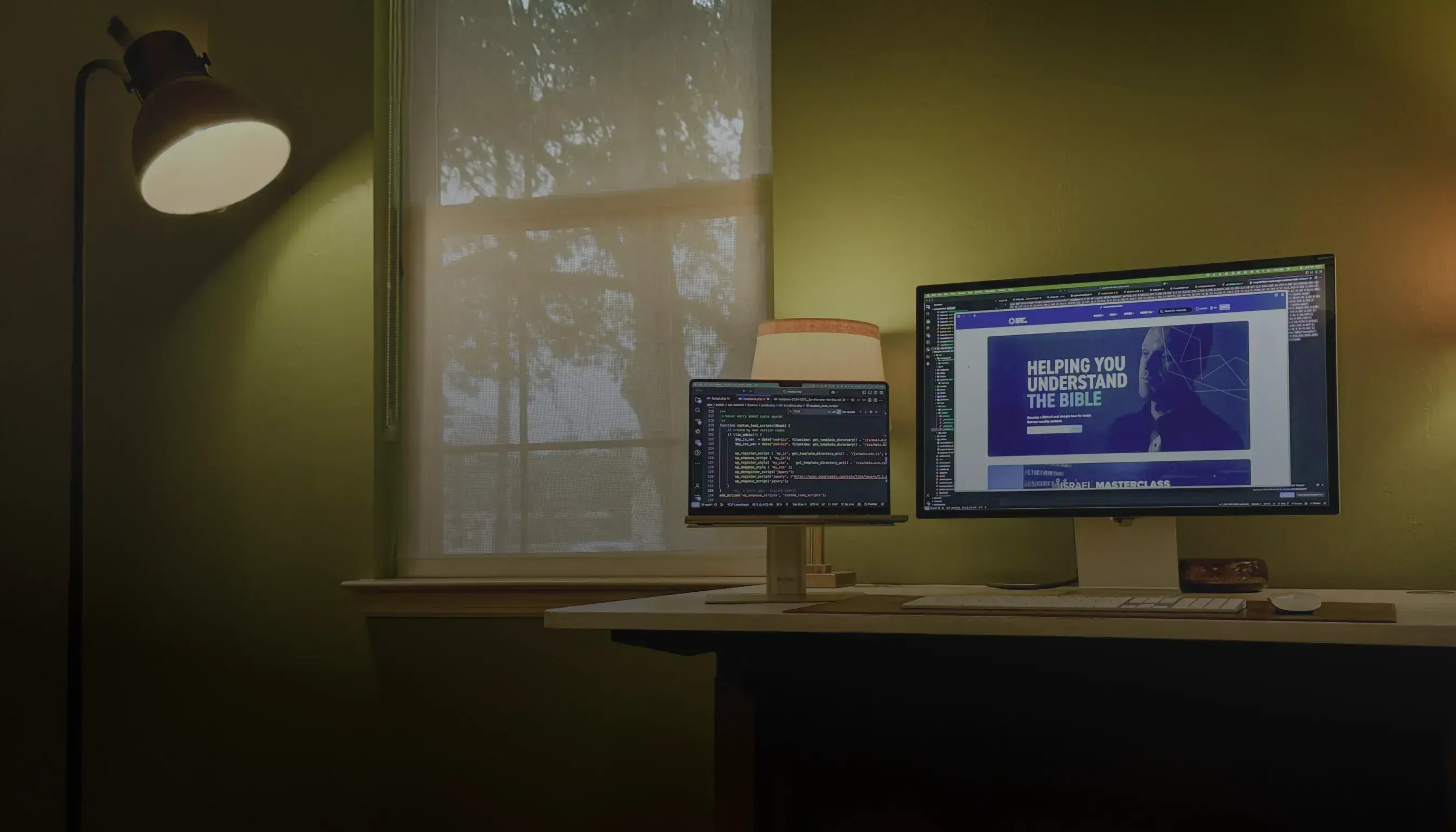 A computer and external monitor sit on a desk with source code on one and the rendered website on the other display