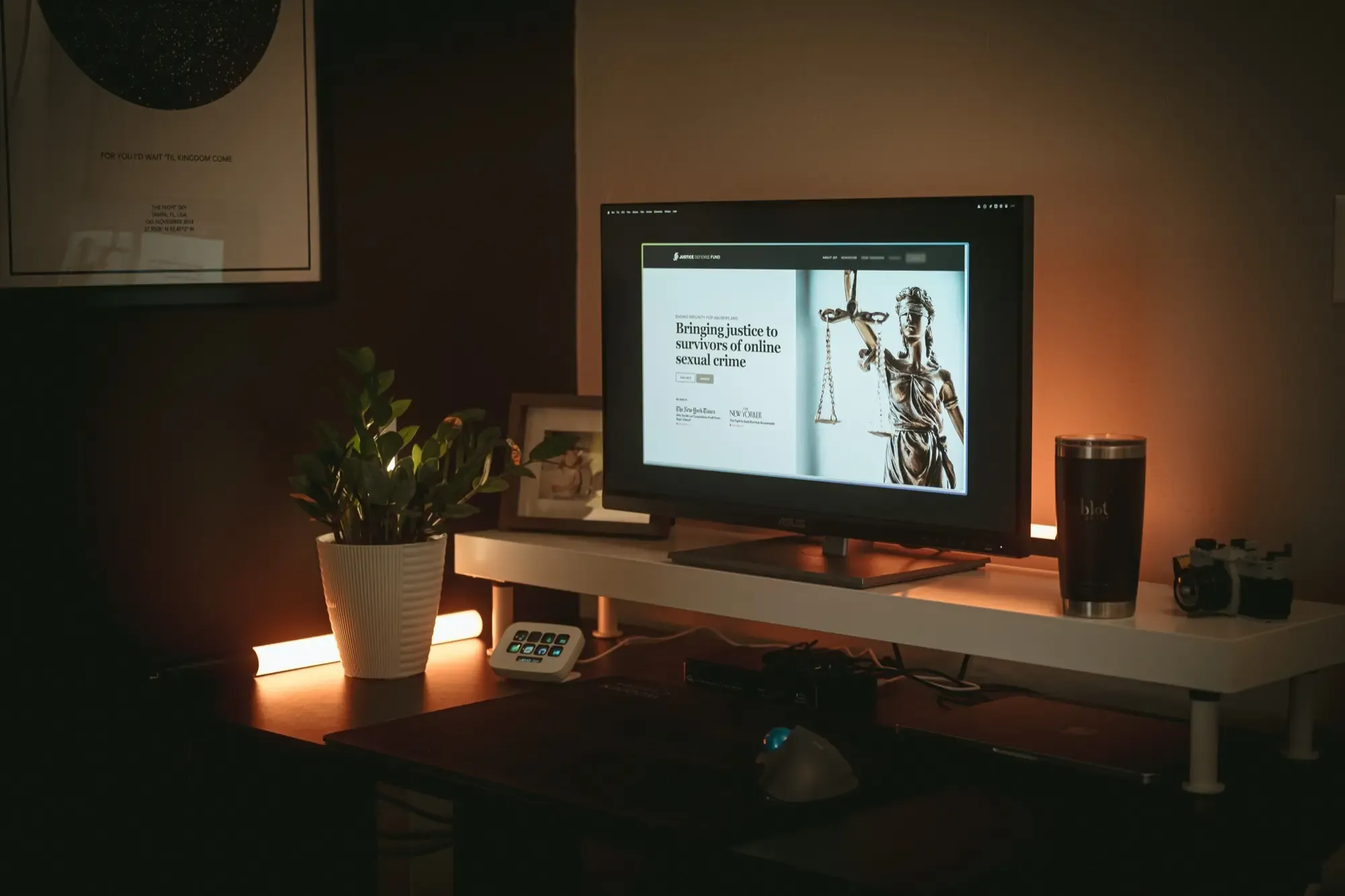 A monitor in a warm dimly lit office shows the Justice Defense Fund website
