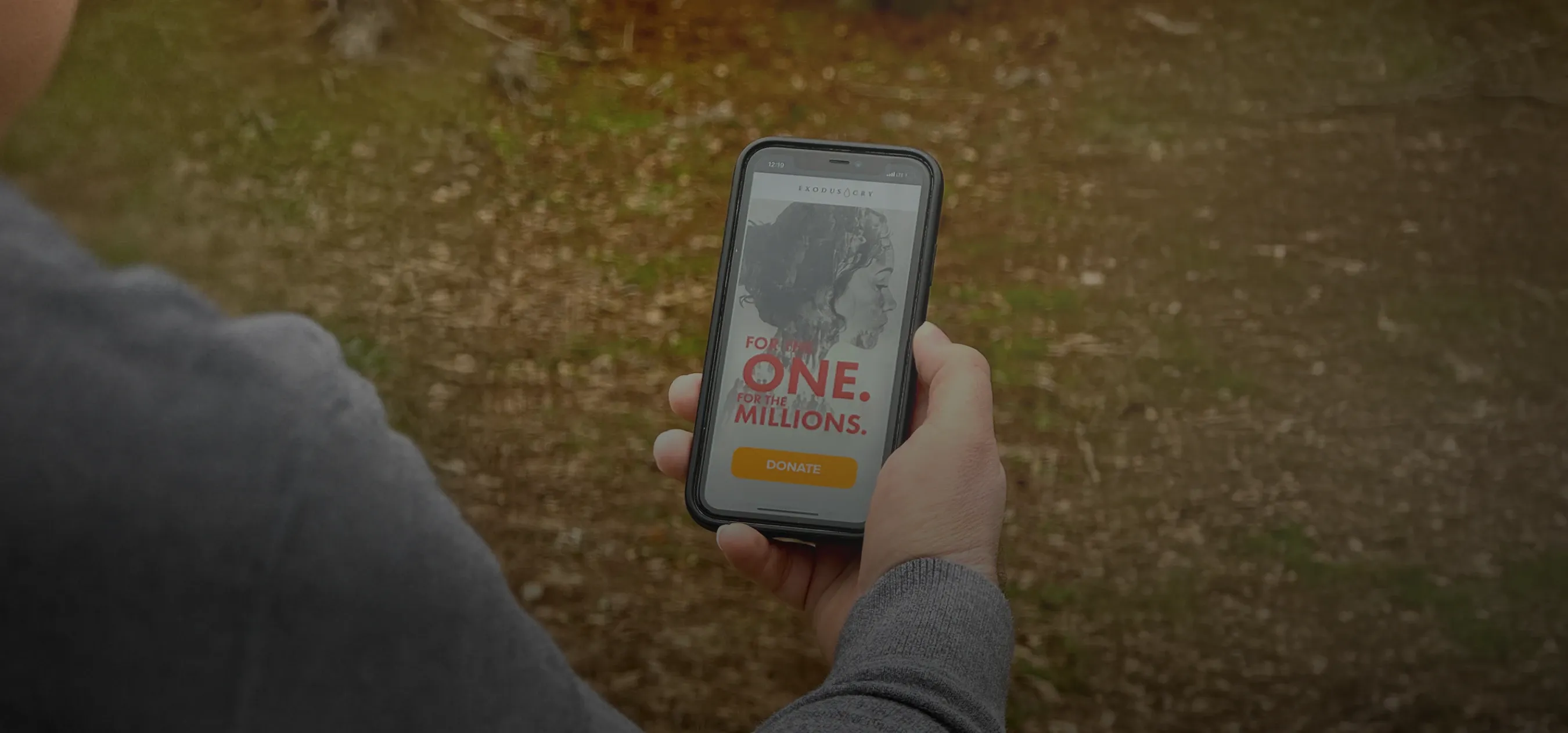 A man hold's an iPhone with a recent end of year campaign on it featuring the words "For the One. For the Millions" and a Donate Now button.