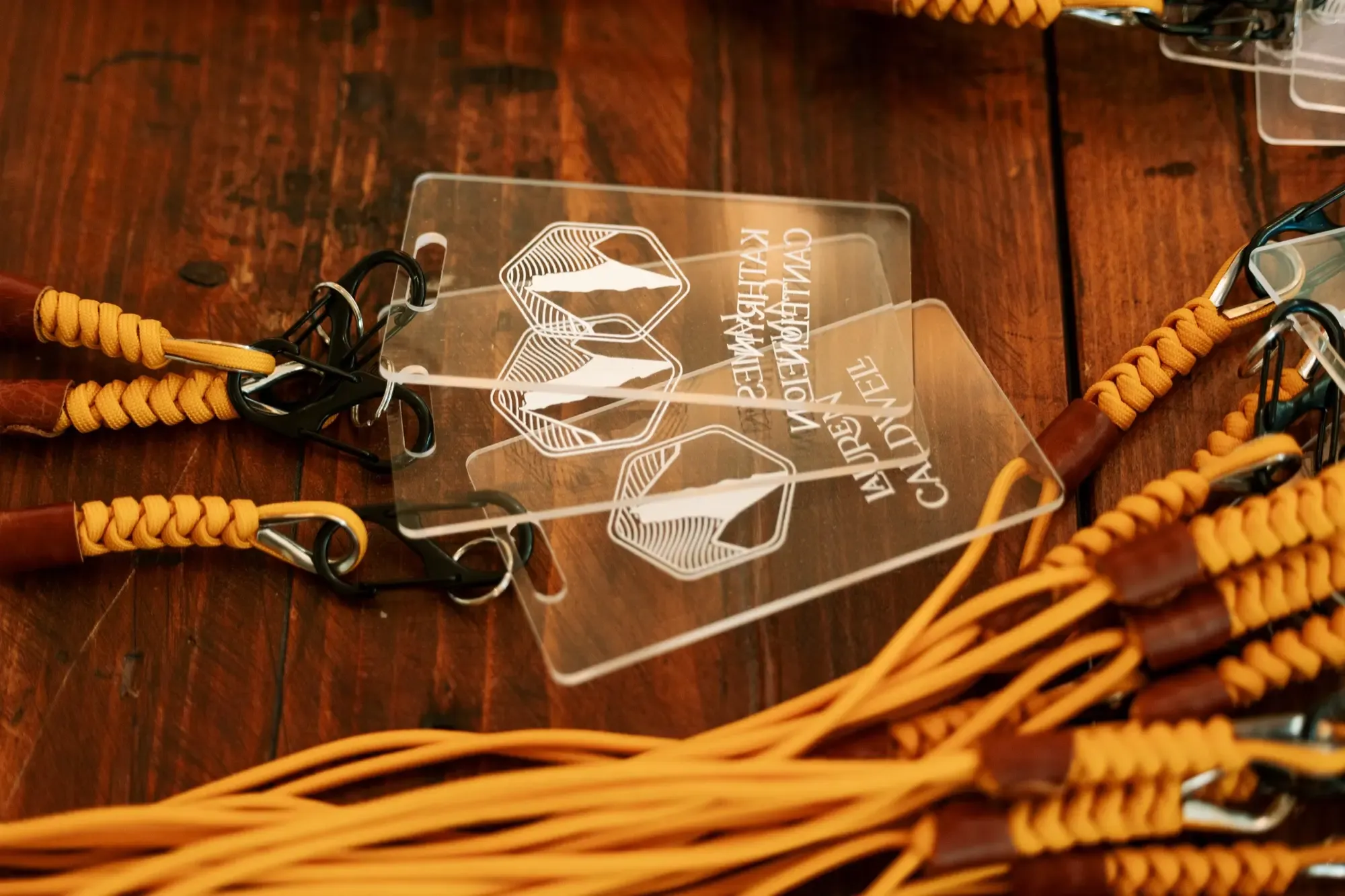 A pile of transparent plastic lanyards with white ink sits atop a wooden desk. The lanyards have yellow straps with fancy leather clasps.